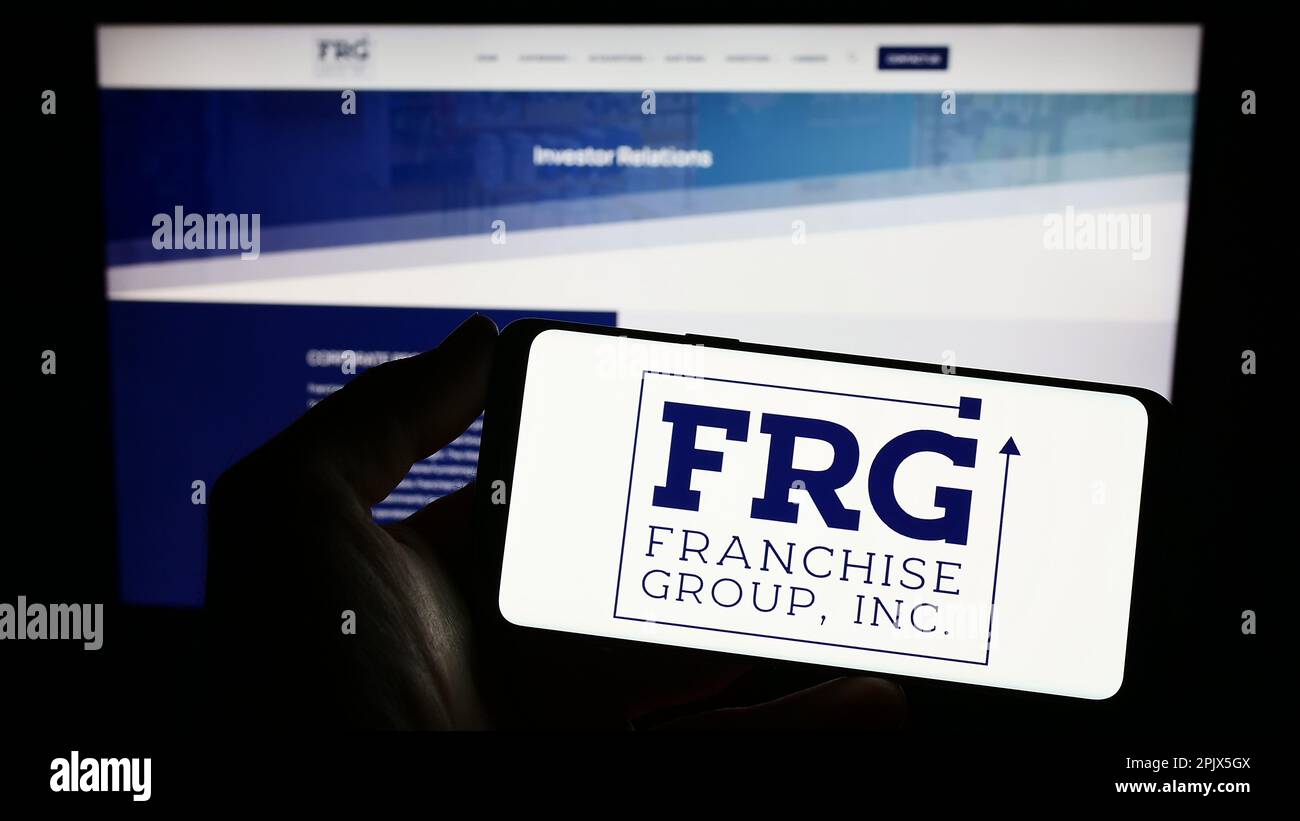 Persona che detiene uno smartphone con il logo della società statunitense Franchise Group Inc. (FRG) sullo schermo davanti al sito Web. Messa a fuoco sul display del telefono. Foto Stock