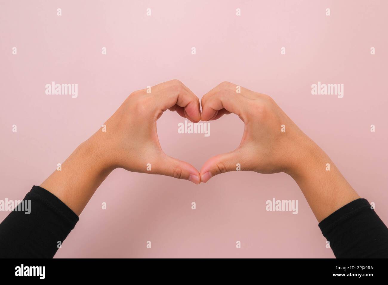Le mani femminili fanno il simbolo del cuore isolato su sfondo rosa con spazio di copia. Love Concept per San Valentino. Foto Stock