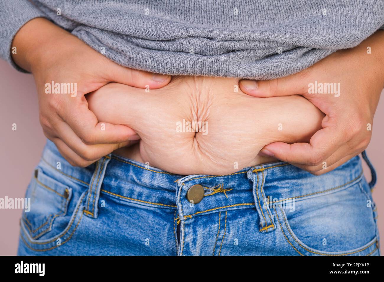 Mano di donna grassa che tiene grasso eccessivo della pancia isolato su sfondo rosa. Pancia grassa in sovrappeso della donna. Dieta femminile e concetto di salute del corpo Foto Stock