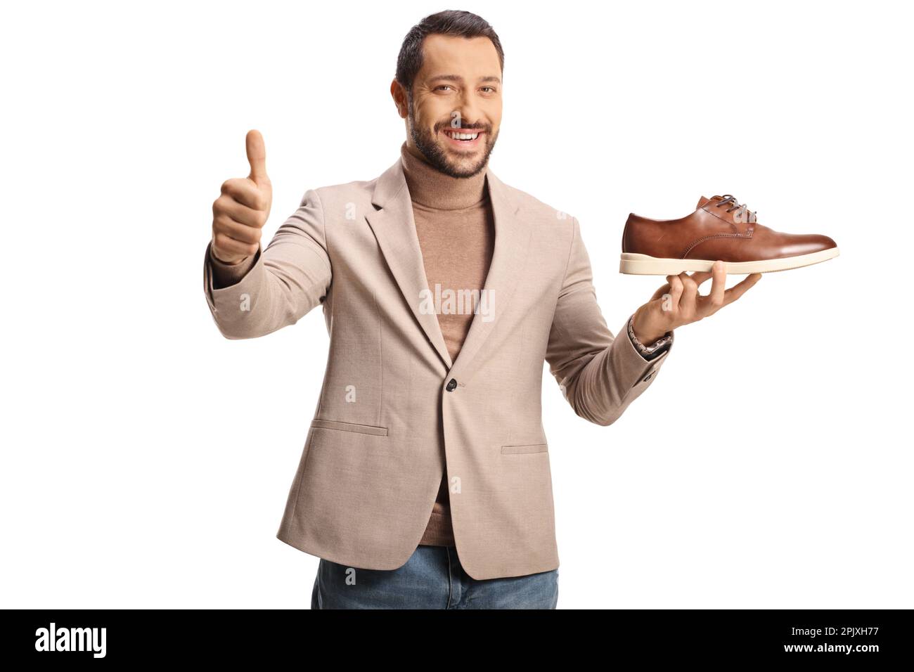 Giovane uomo che tiene una scarpa in pelle marrone e gesturando pollici isolato su sfondo bianco Foto Stock