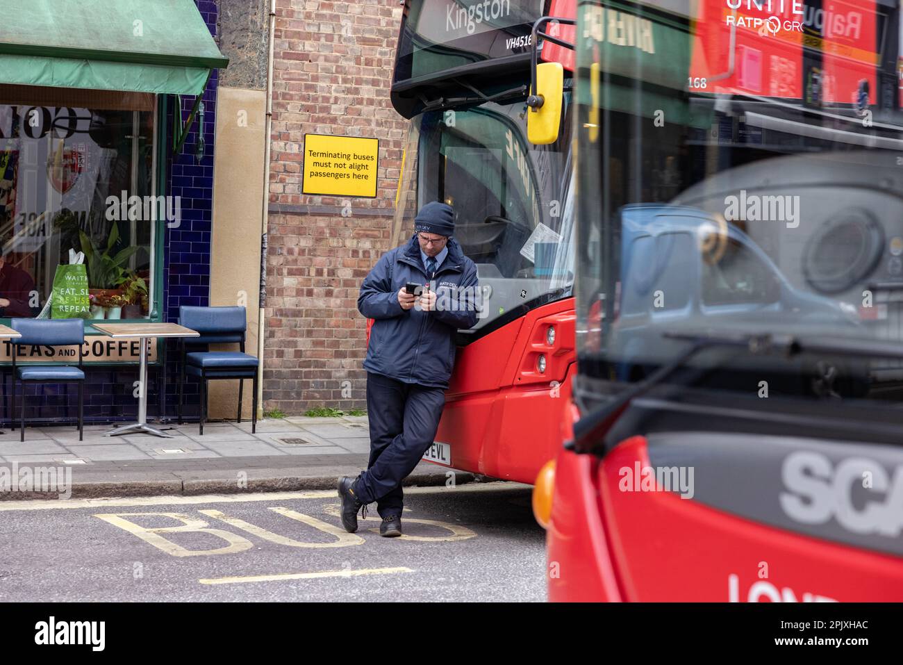 L'autista dell'autobus di Londra si prende una pausa mentre fa una pausa mentre si appoggia sul suo autobus parcheggiato alla stazione di Putney Bridge, Southwest London, Inghilterra, Regno Unito Foto Stock