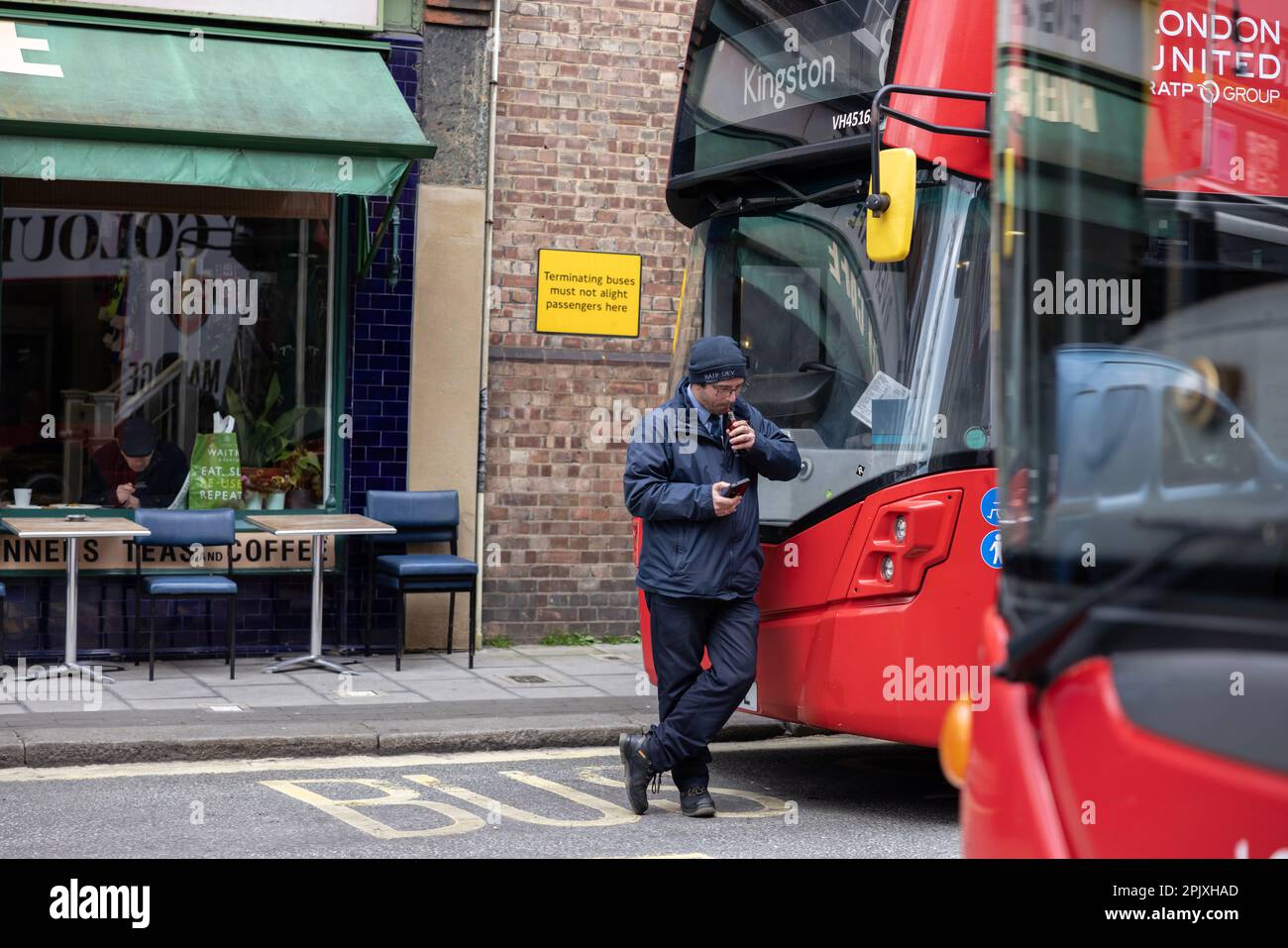 L'autista dell'autobus di Londra si prende una pausa mentre fa una pausa mentre si appoggia sul suo autobus parcheggiato alla stazione di Putney Bridge, Southwest London, Inghilterra, Regno Unito Foto Stock