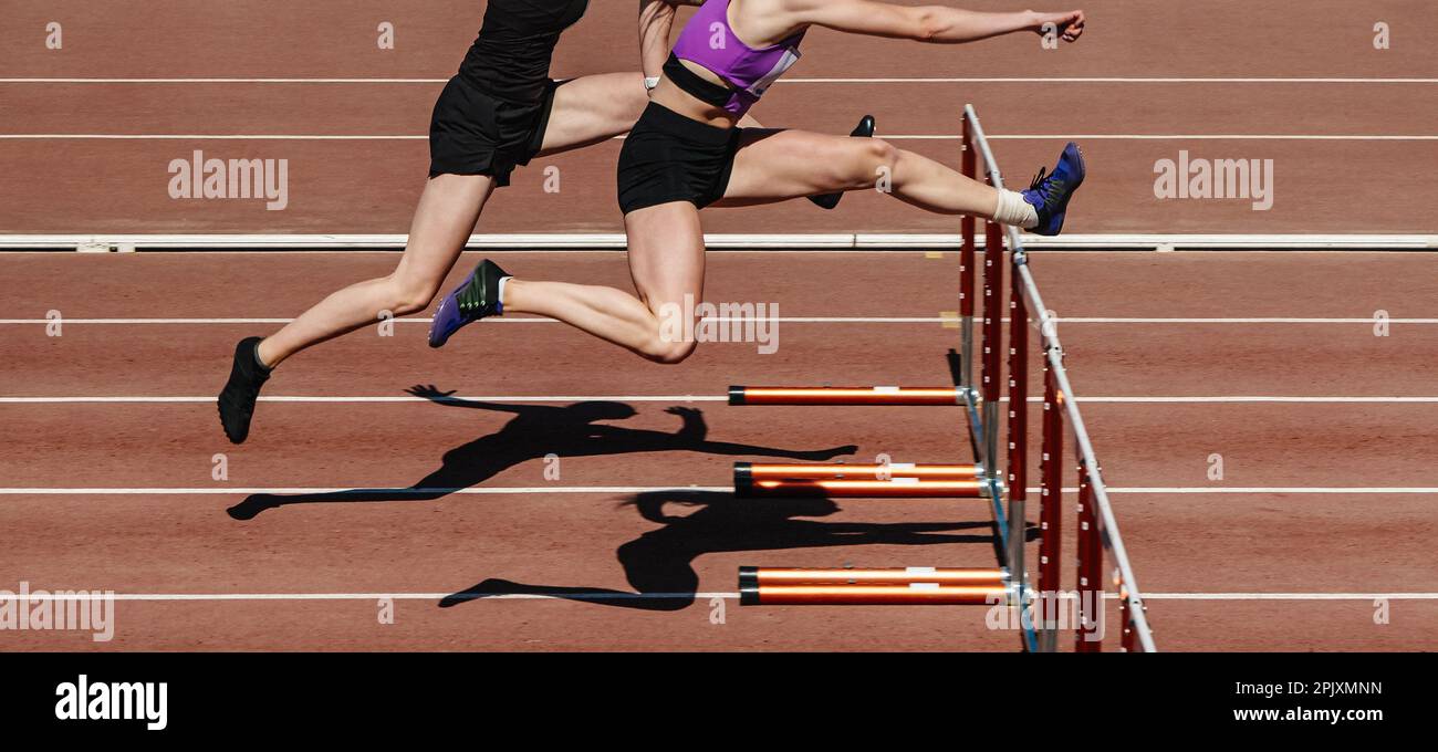 due atlete che corrono a ostacoli nella competizione di atletica, che corrono a ostacoli sulla pista dello stadio, giochi sportivi estivi Foto Stock