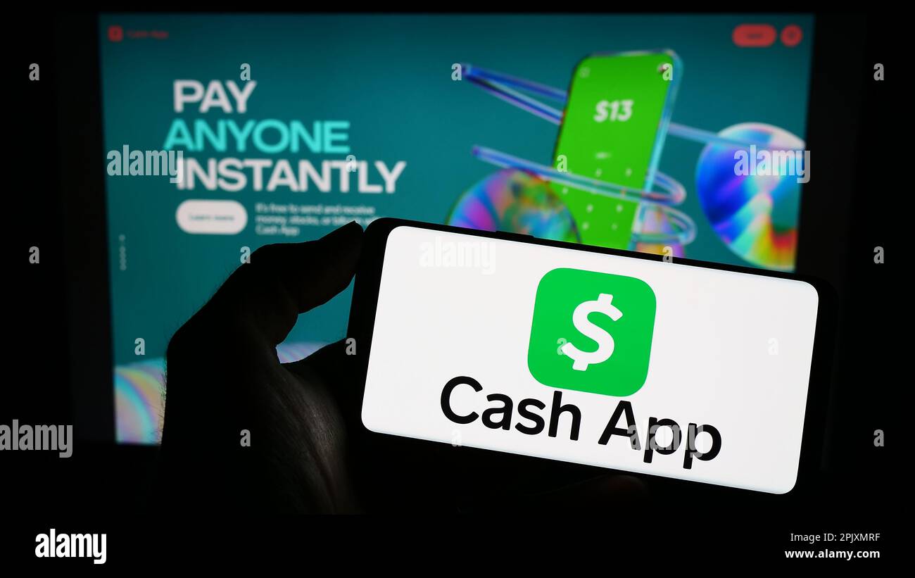 Persona che tiene il telefono cellulare con il logo della società americana fintech Cash App Investing LLC sullo schermo di fronte alla pagina web. Messa a fuoco sul display del telefono. Foto Stock