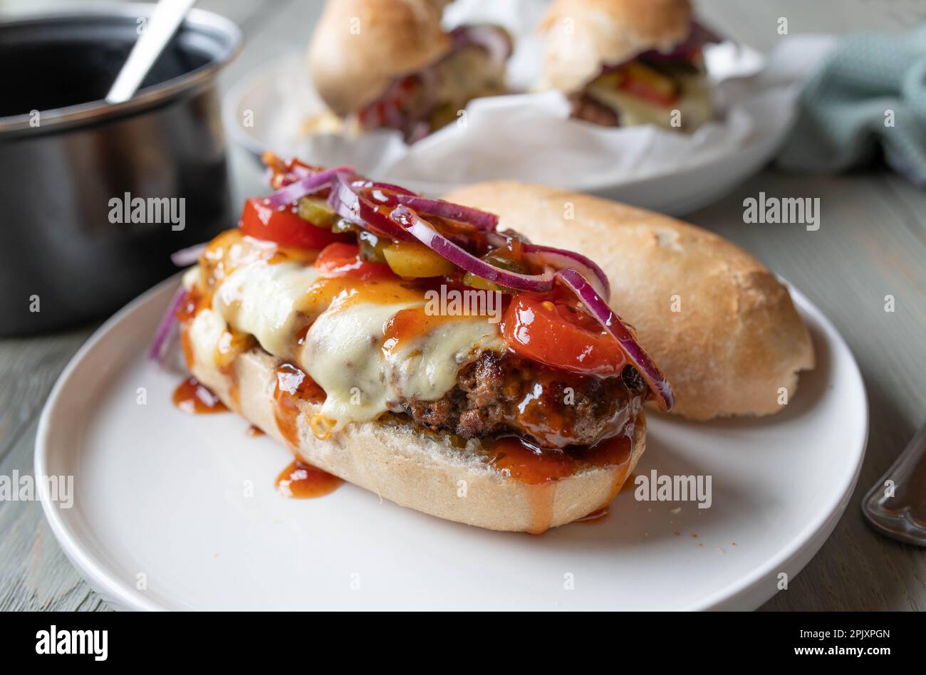 Panino cheeseburger con pomodori, sottaceti, cipolle e salsa al barbecue su un panino baguette Foto Stock