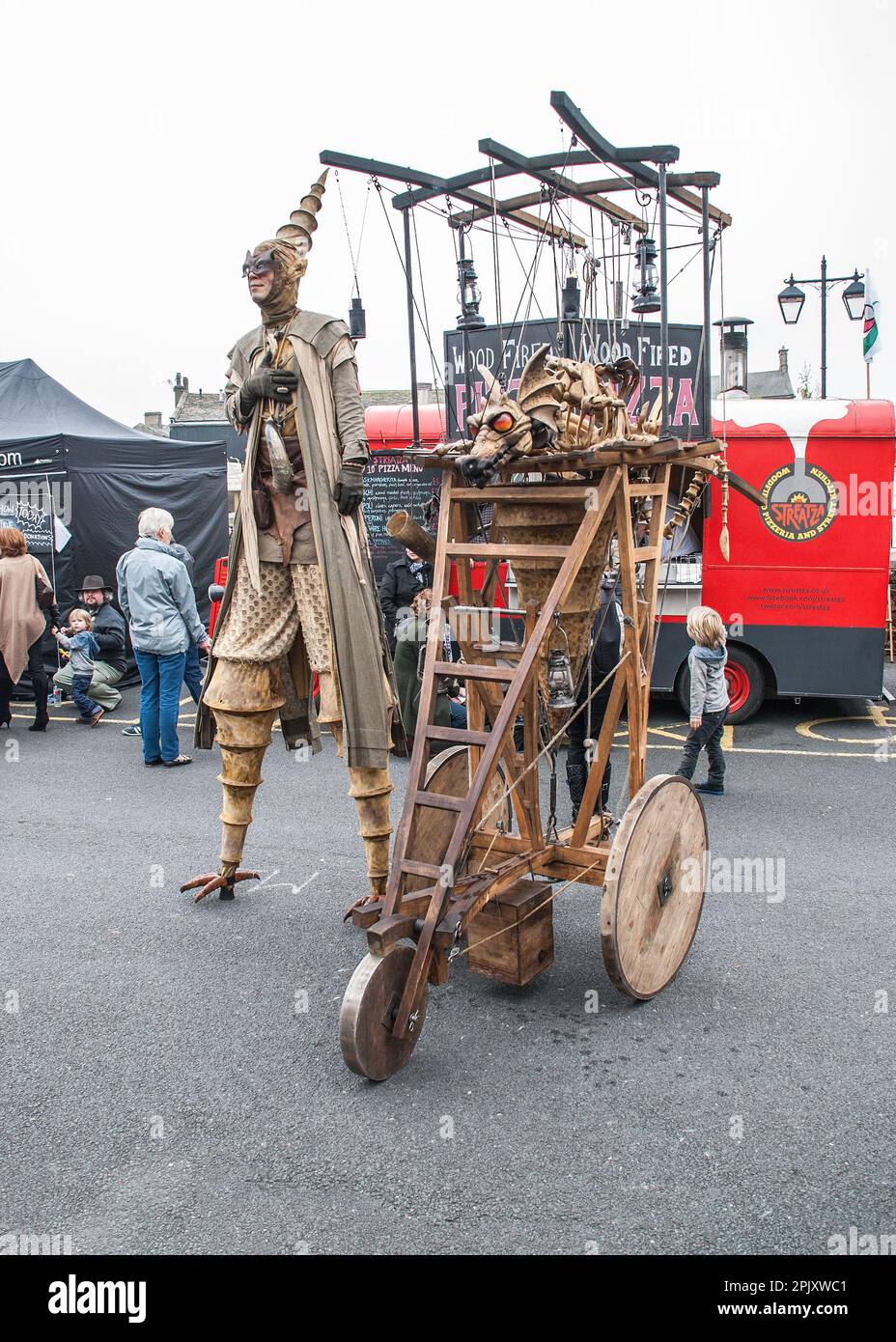 Persona su palafitte con un contraption mobile che sport un drago di respirazione del fuoco, visto al festival internazionale dei burattini di Skipton circa 2015. Foto Stock