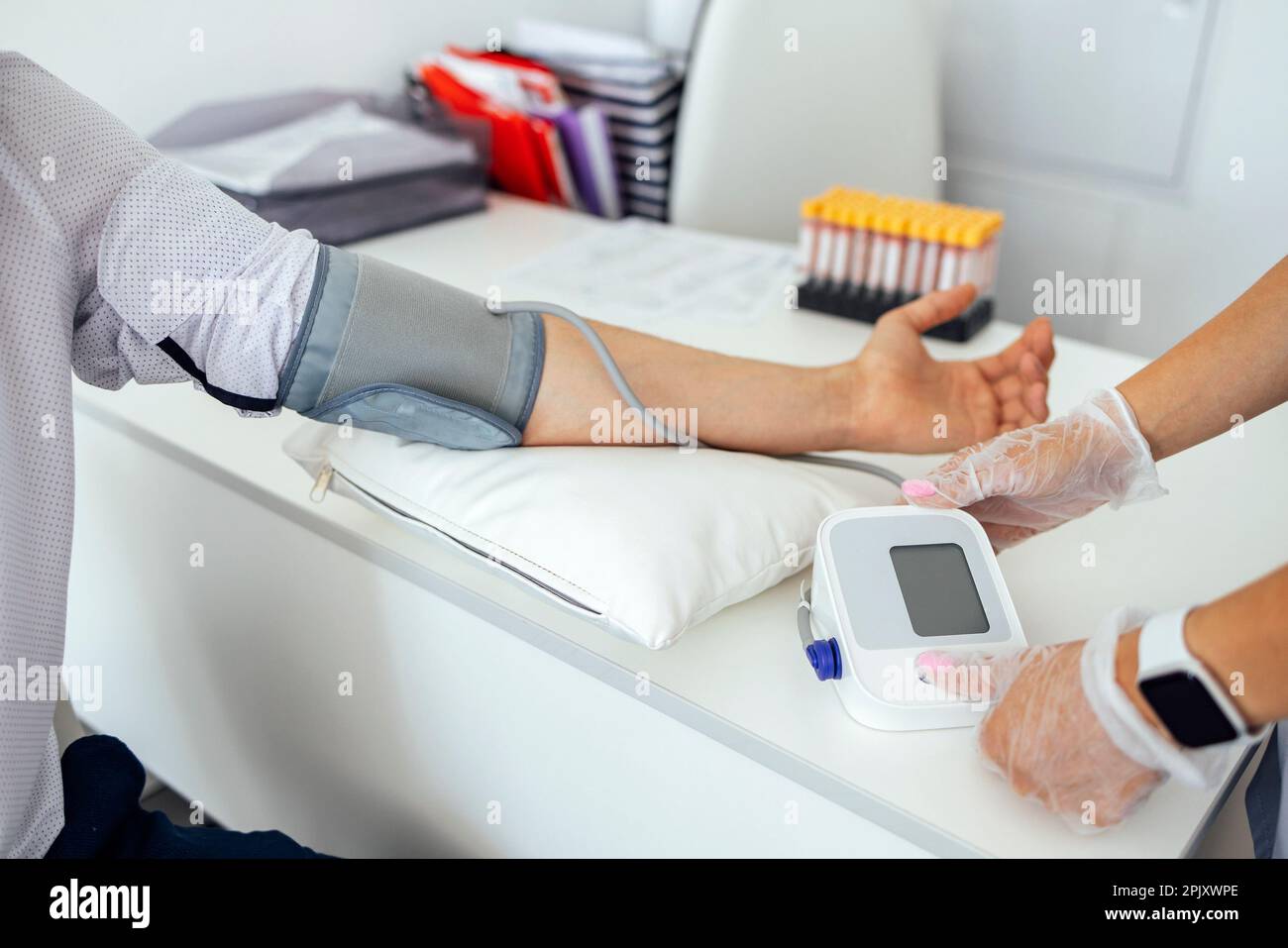 Infermiere in uniforme medica e guanti trasparenti per il controllo della pressione sanguigna di un giovane uomo in abiti casual. La donna della brunetta preme il tasto sul tonometro. Te Foto Stock