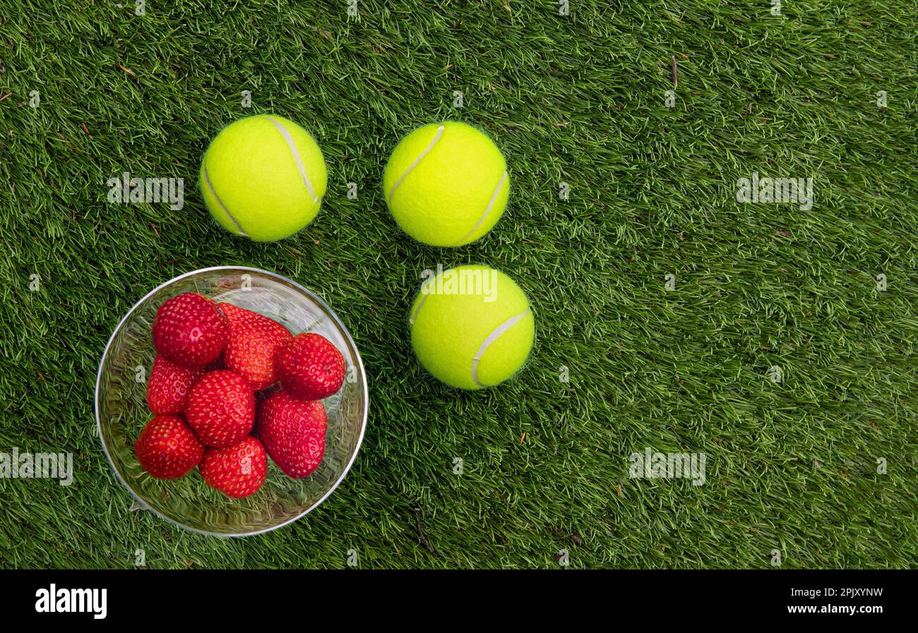 3 palla da tennis e un bicchiere con fragole su erba. Foto Stock