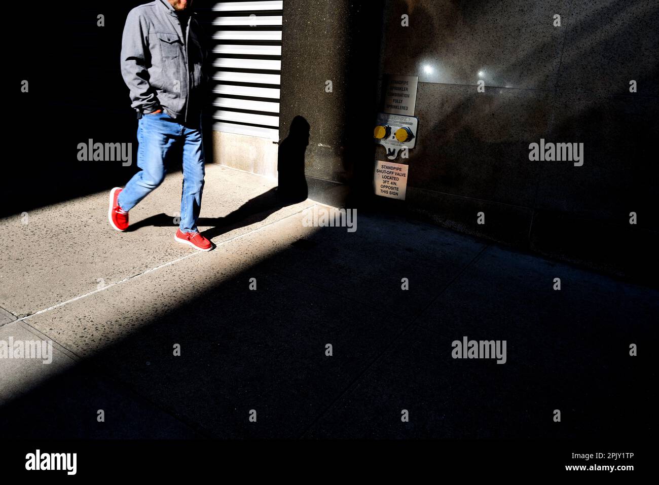 Uomo che cammina attraverso la luce su una strada di New York City Foto Stock