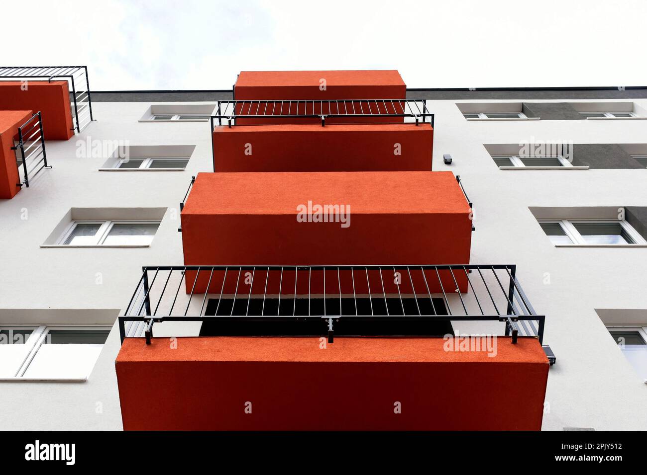 serie di balconi in stucco rosso testurizzato che guardano in prospettiva. edificio residenziale con vista dall'esterno. finestre bianche. architettura moderna Foto Stock