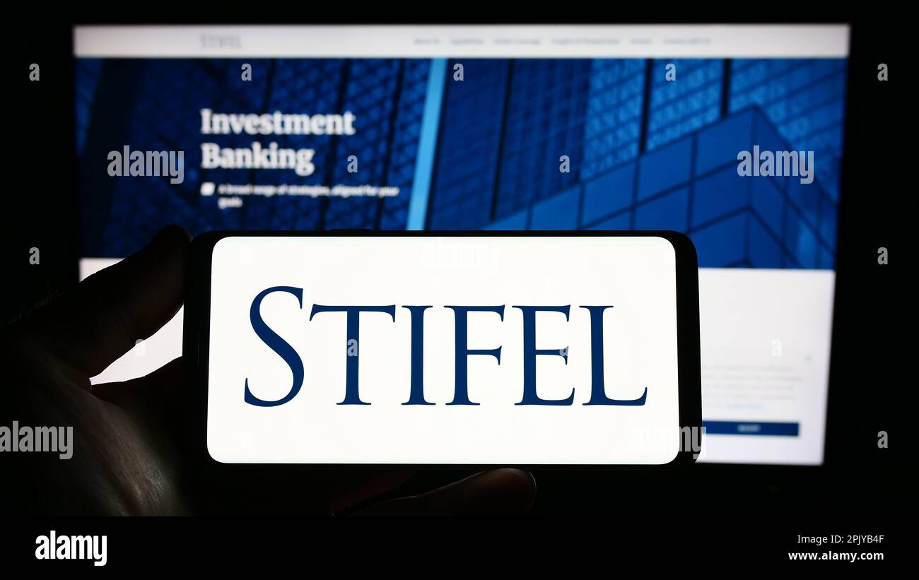 Persona in possesso di smartphone con il logo della società di investimento statunitense Stifel Financial Corp. Sullo schermo di fronte al sito Web. Messa a fuoco sul display del telefono. Foto Stock