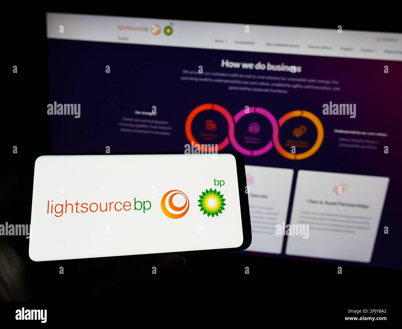 Persona che tiene il cellulare con il logo della compagnia britannica di energia rinnovabile Lightsource BP sullo schermo di fronte alla pagina web. Messa a fuoco sul display del telefono. Foto Stock