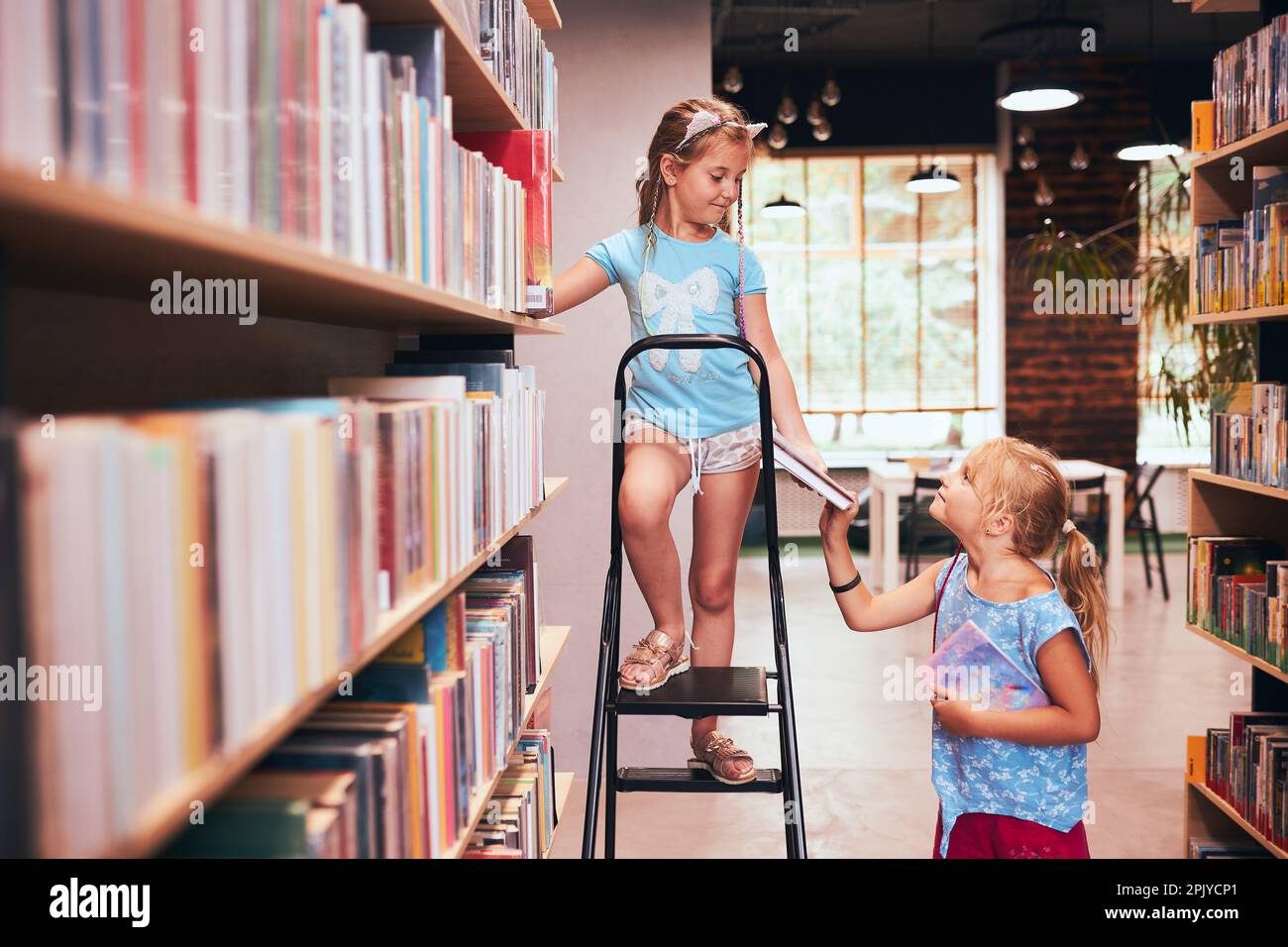 Due scolaresche che scelgono libri nella biblioteca scolastica. Studenti della scuola elementare che imparano dai libri. I bambini si divertono nel club scolastico. Ritorno a scuola. Doi Foto Stock