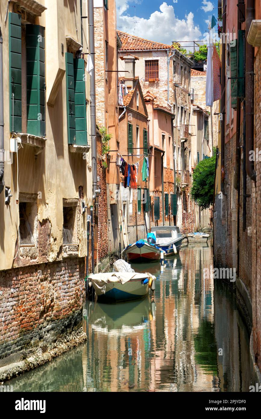 Vista romantica di una vecchia strada stretta sull'acqua, un canale con vecchie case e barche in una giornata di sole a Venezia Foto Stock