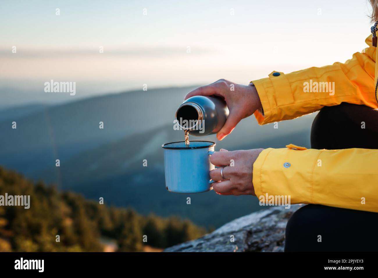 Donna turista che versa una bevanda calda dai thermos nella tazza di viaggio in montagna. Rinfresco durante le escursioni all'aperto Foto Stock