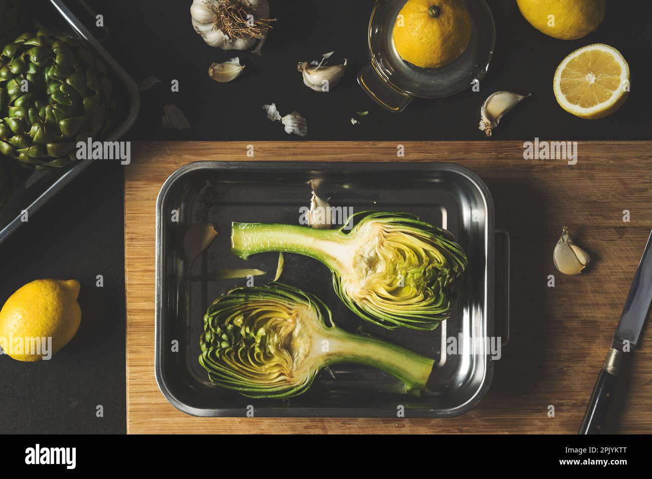 Fiore di carciofo tagliato a metà in una teglia da forno, preparazione degli alimenti per la cottura, ricetta per la cottura dei carciofi, shot vista dall'alto Foto Stock