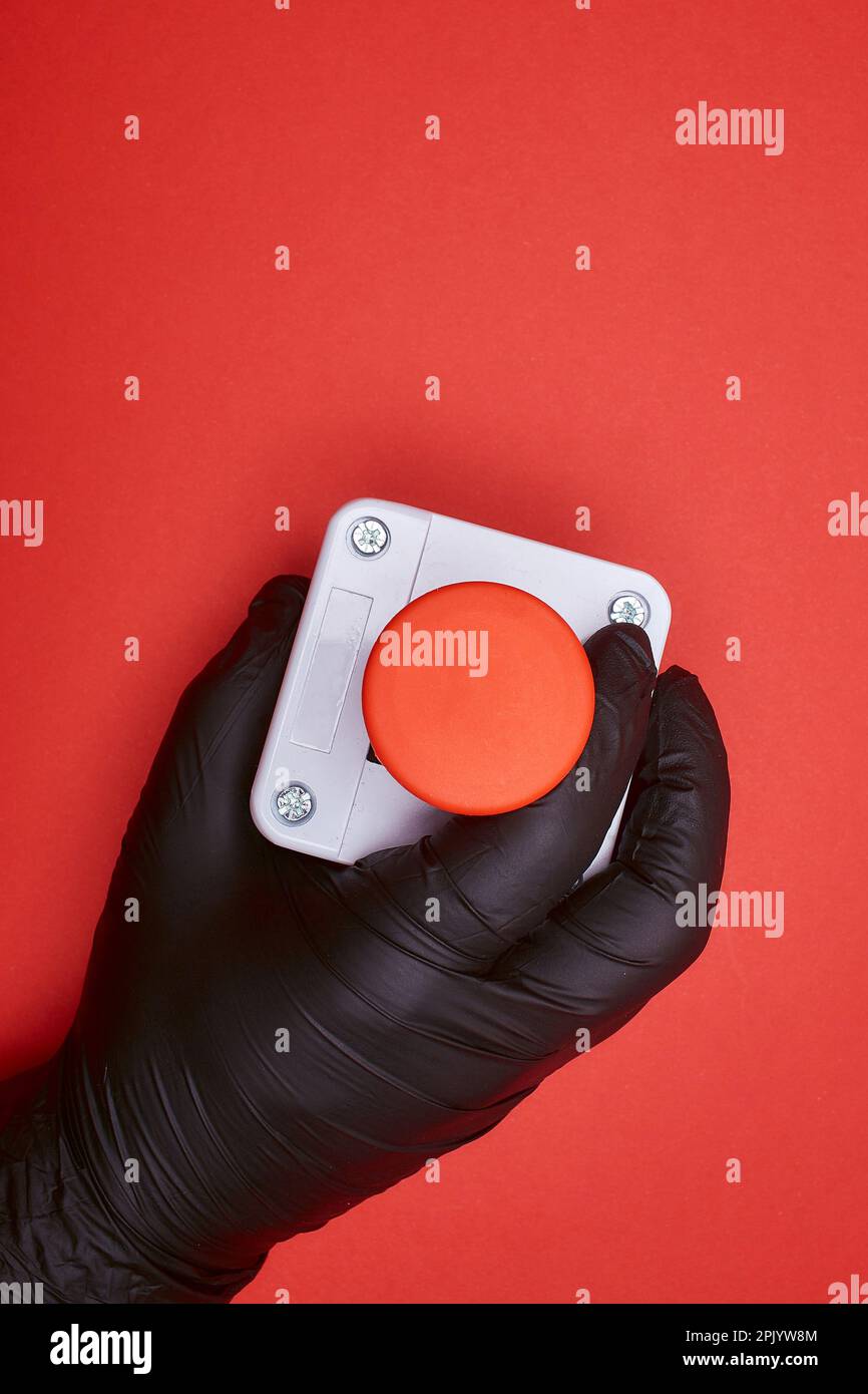La mano nel guanto in resina nera, che stringe il pulsante di emergenza sullo sfondo rosso nella vista dall'alto Foto Stock