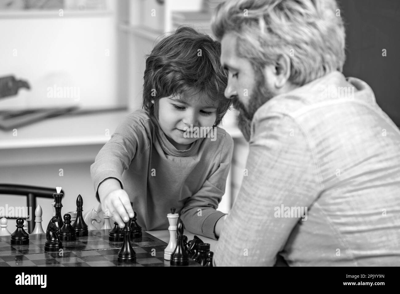 Bell'insegnante che dà lezioni private di scacchi al ragazzo prescolare. Padre insegna a suo figlio a giocare a scacchi. Ragazzi intelligenti. Foto Stock