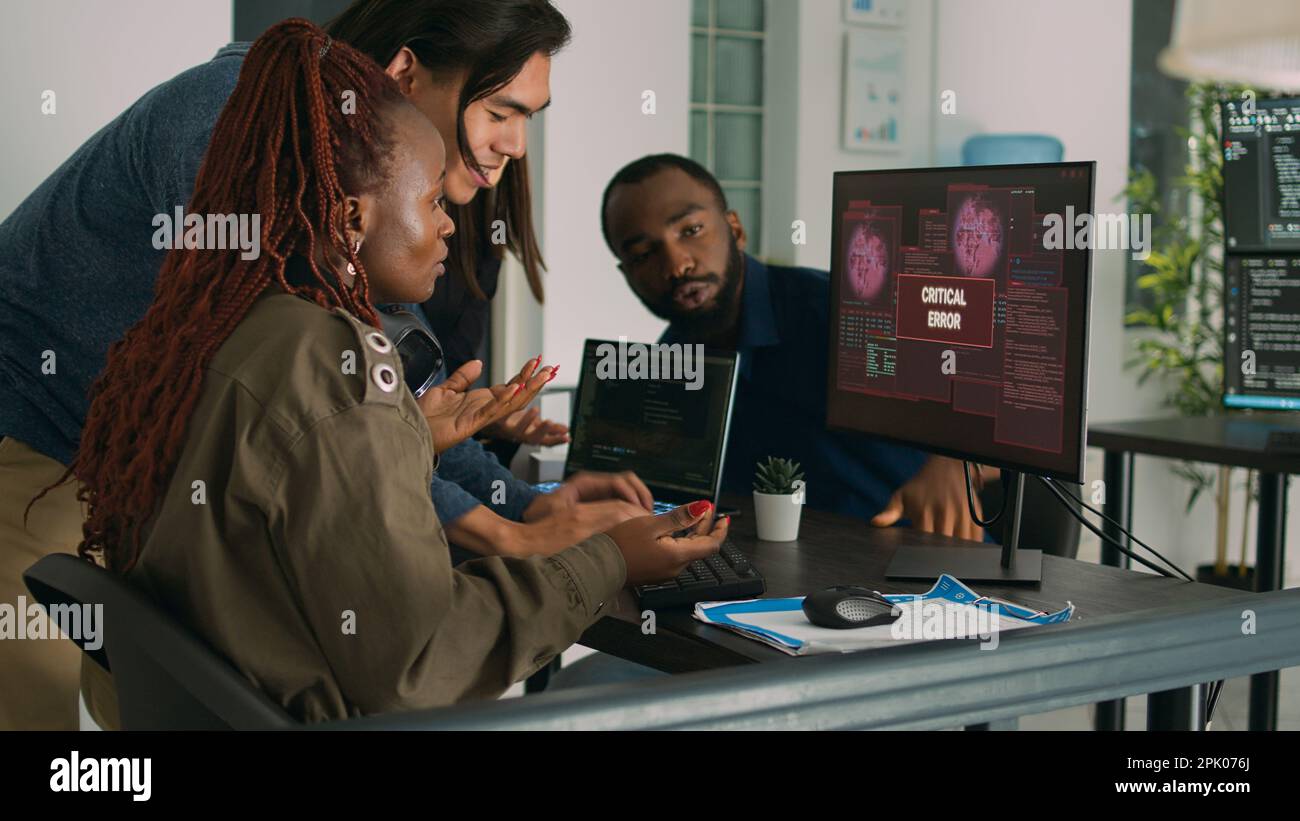 Gruppo multietnico di ingegneri IT che si occupano dell'avviso di hacking, visualizzando l'errore del server di sicurezza sul computer. Sviluppatori di software che hanno violato computer e sistema, lavorando su database. Foto Stock
