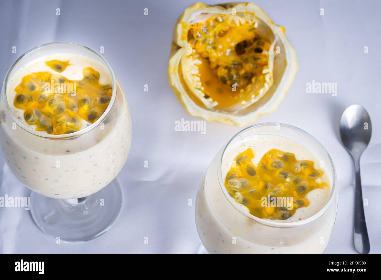 Mousse di frutto della passione in una ciotola di vetro, con frutto della passione sullo sfondo, su sfondo bianco. Vista prospettica. Foto Stock