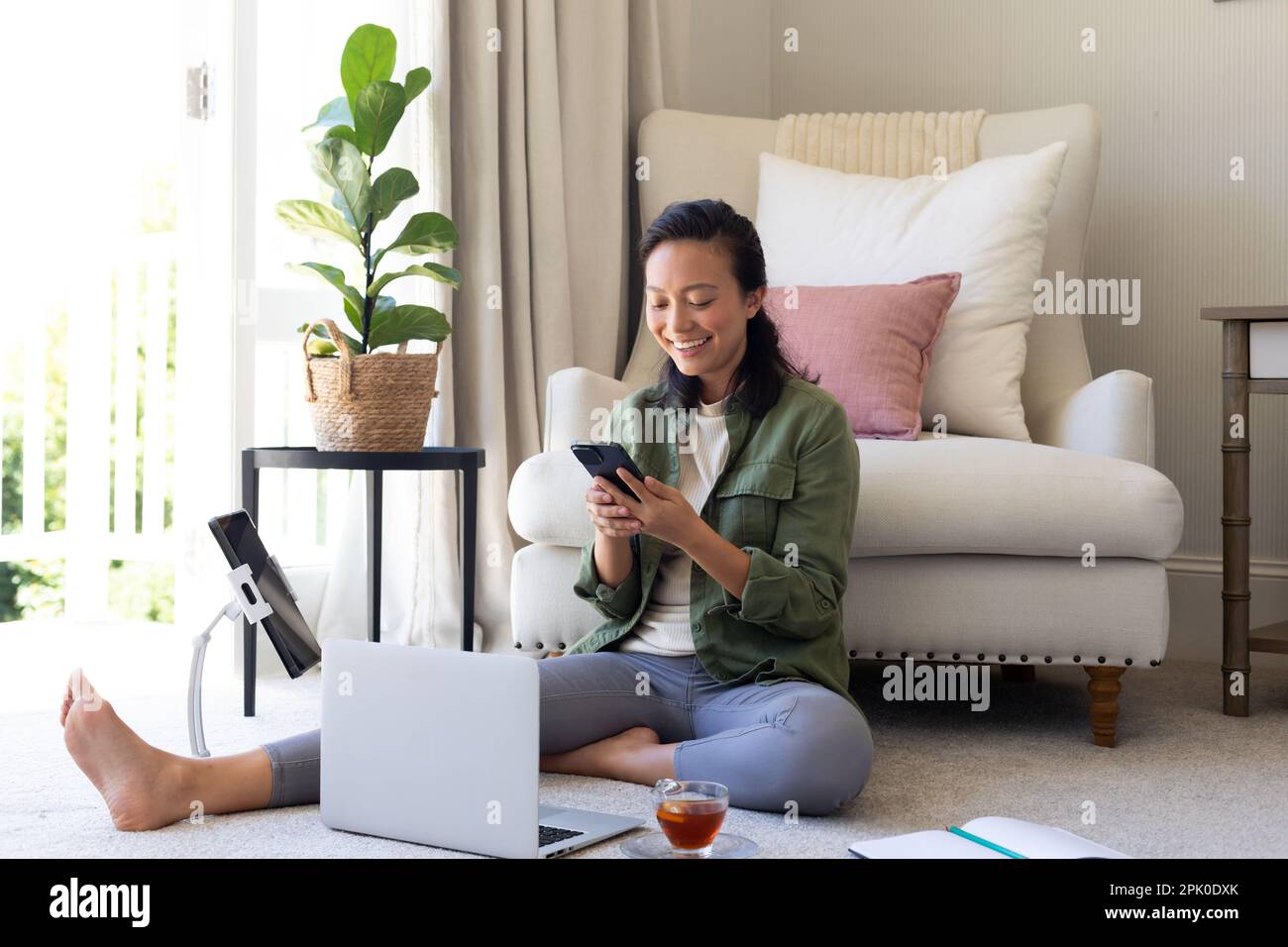 Felice donna asiatica seduta a casa con smartphone, tablet e notebook Foto Stock