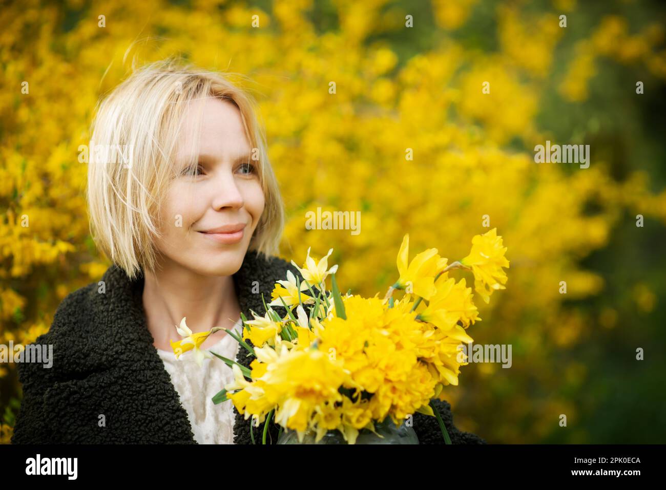 Faccia felice, pensieri leggeri, sogni. Donna su sfondo giallo con fiori gialli. Donna bionda di mezza età sorridente più di quaranta anni. Posiziona per testo. Foto Stock