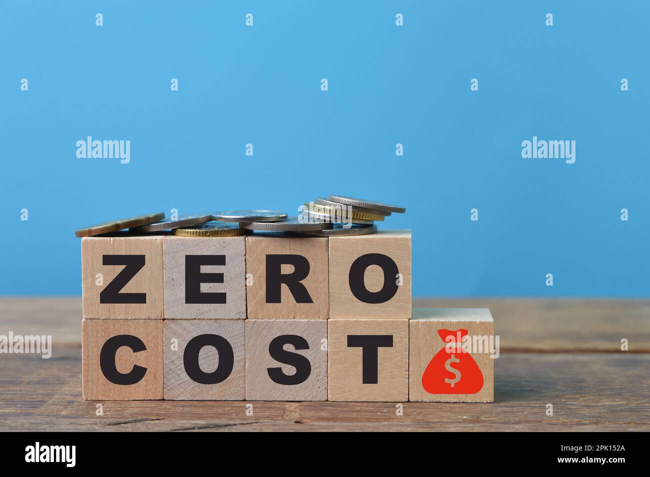 Monete, simboli di denaro e blocchi di legno con testo A COSTO ZERO Foto Stock