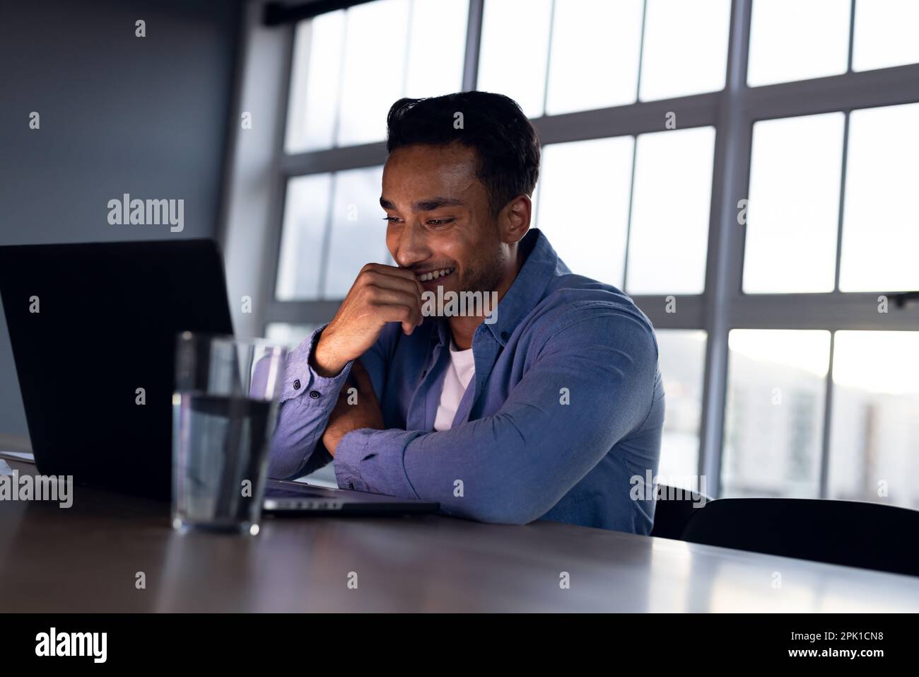 Buon uomo d'affari biraciale seduto alla scrivania e con un computer portatile, che lavora tardi in ufficio Foto Stock