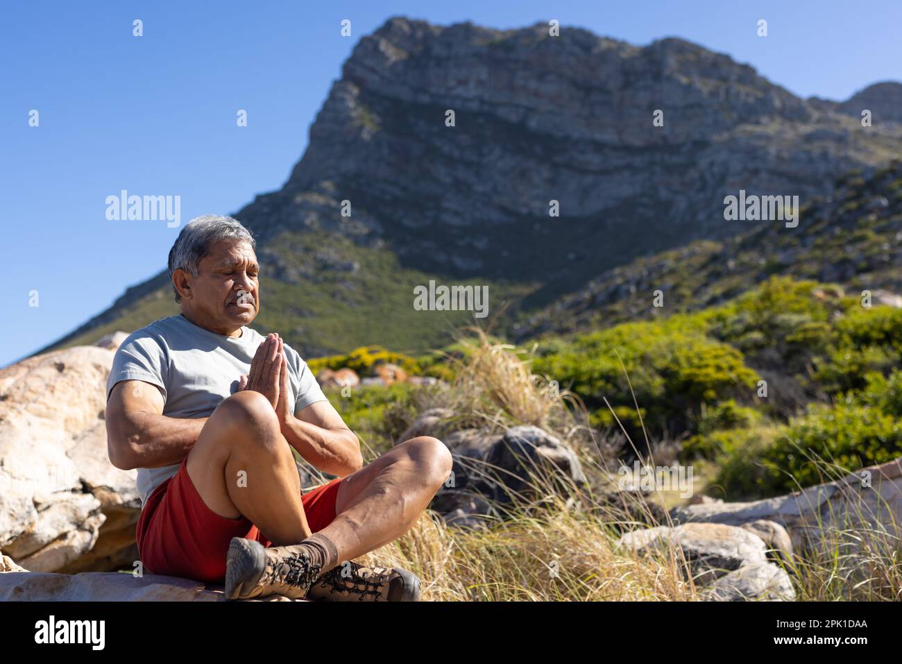 Uomo anziano biraciale che fa yoga e medita in montagna Foto Stock