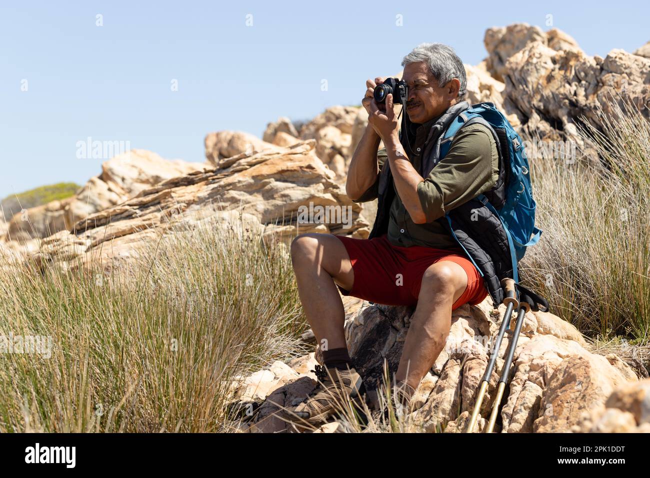 Felice uomo biraciale anziano che indossa lo zaino, escursioni in montagna, scattare foto con la fotocamera Foto Stock