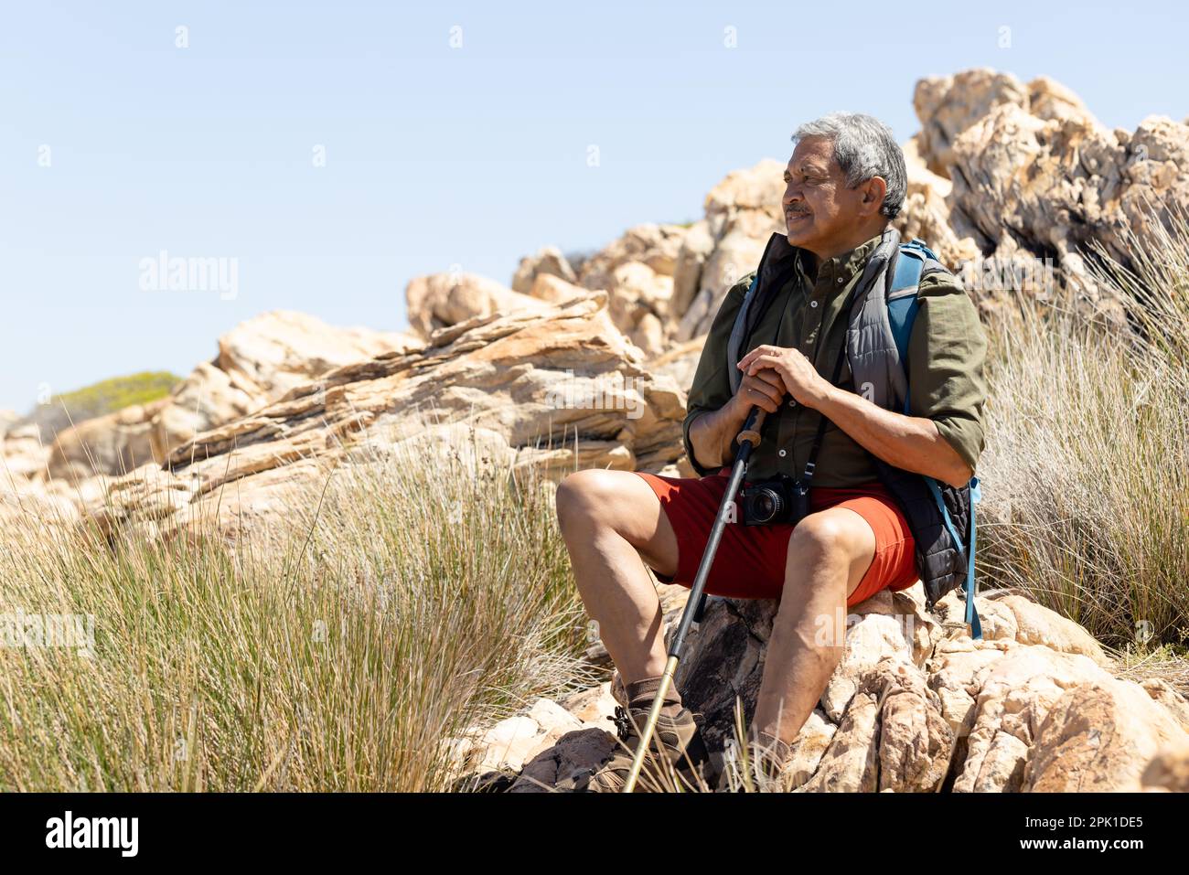 Felice uomo biraciale anziano che indossa zaino, escursioni in montagna, seduta sulla roccia Foto Stock