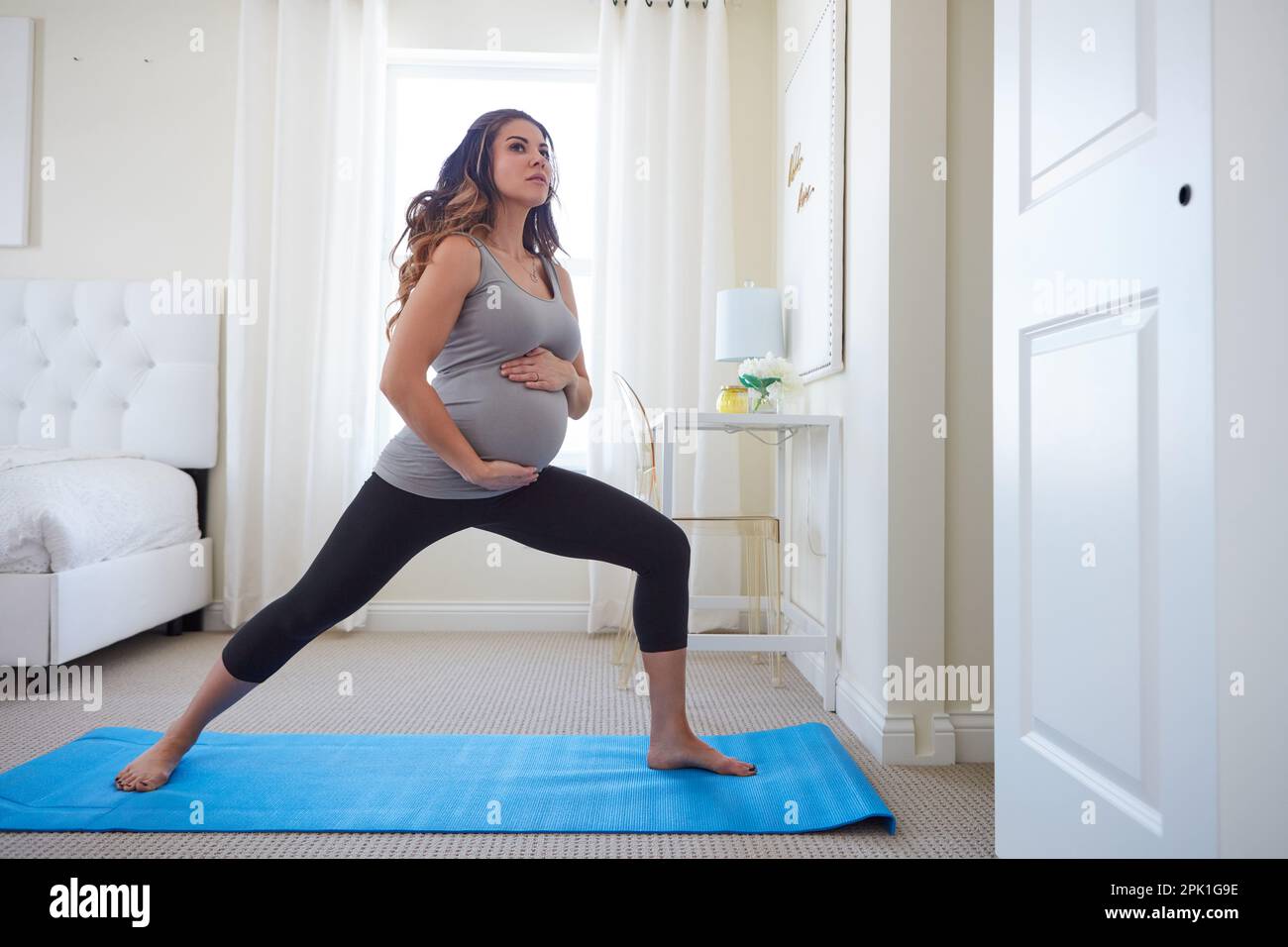 Mamma aka il guerriero originale. una giovane donna incinta che pratica una routine di yoga a casa. Foto Stock