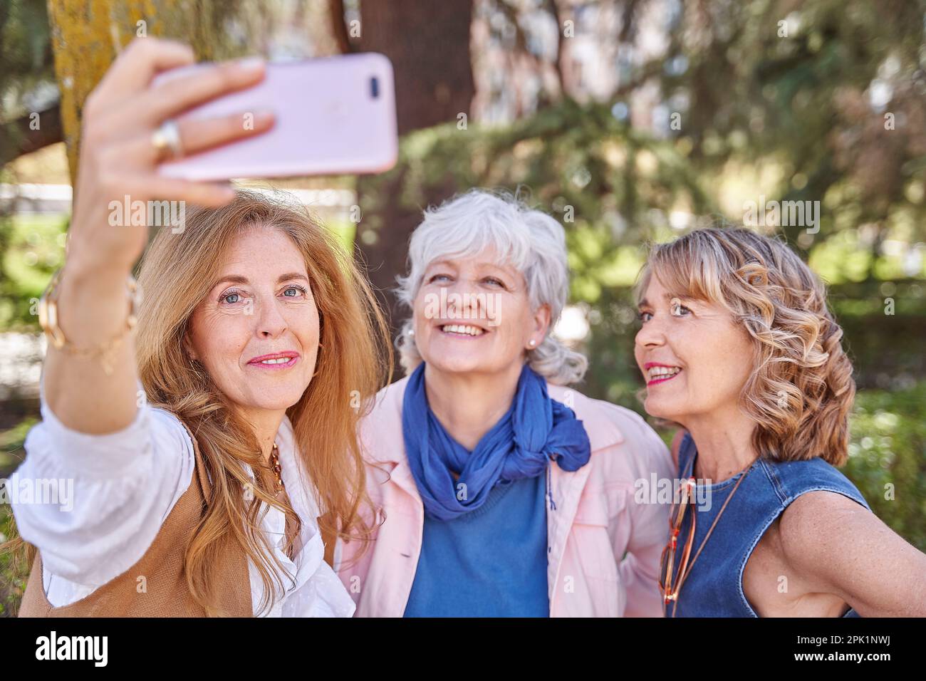Tre donne anziane condividono un momento divertente prendendo un selfie con il loro telefono, dimostrando che l'età è solo un numero quando si tratta di creare ricordi Foto Stock