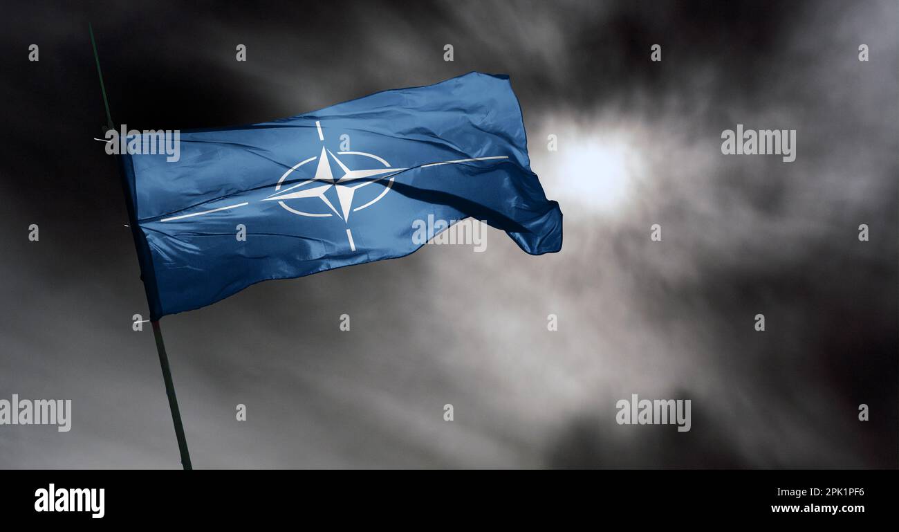Bandiera della NATO che sventola al vento su un paletto contro il cielo Foto Stock