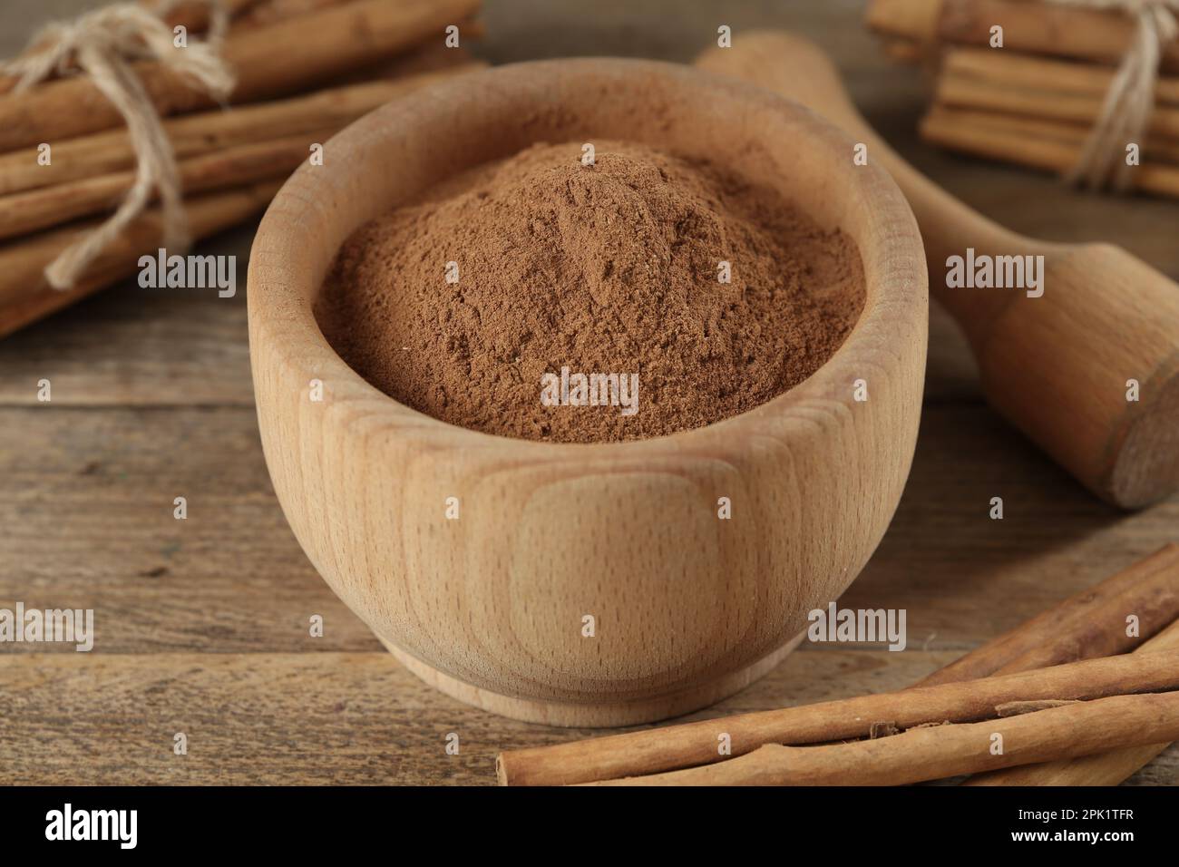Cannella in polvere aromatica in mortaio, bastoncini e pestello su tavola di legno, primo piano Foto Stock