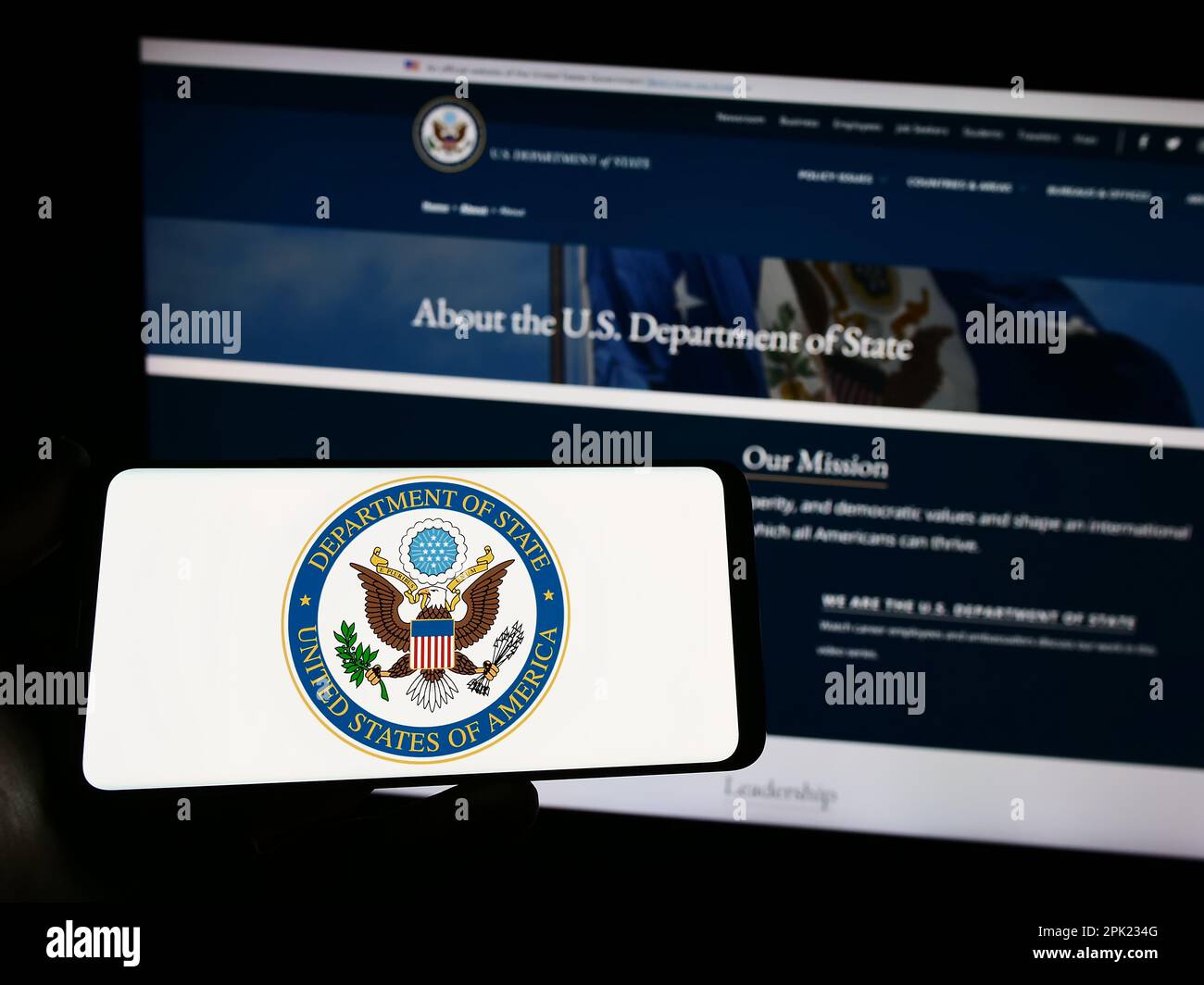 Persona che tiene lo smartphone con il sigillo del Dipartimento di Stato degli Stati Uniti (DOS) sullo schermo di fronte al sito Web. Messa a fuoco sul display del telefono. Foto Stock