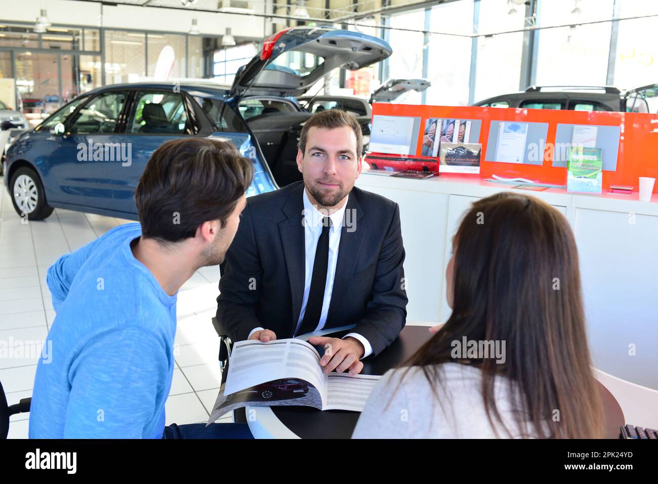 Coppia giovane l'acquisto di una nuova auto nello showroom di una concessionaria auto - firma del contratto di vendita con il venditore Foto Stock