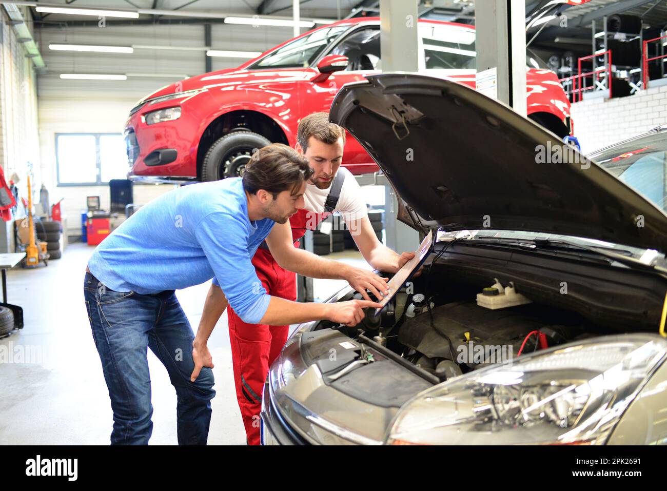 Servizio di assistenza post-vendita in riparazione auto shop - meccanico e l'uomo parla di riparazione di un veicolo Foto Stock