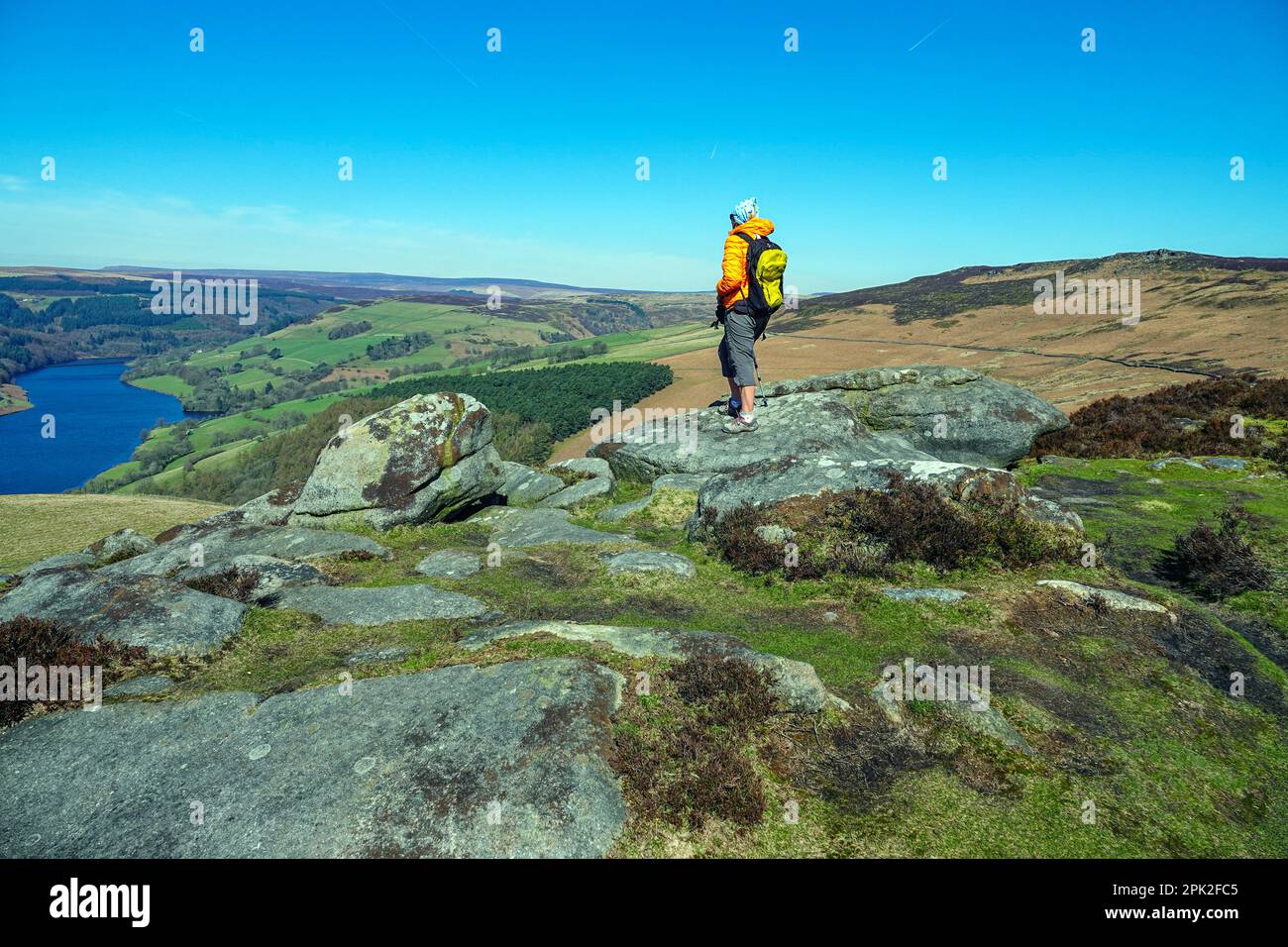 Escursionista femminile camminando lungo Dovestones Edge, sopra il lago artificiale di Ladybower e le dighe di Derwent, Peak District, Derbyshire, Regno Unito Foto Stock