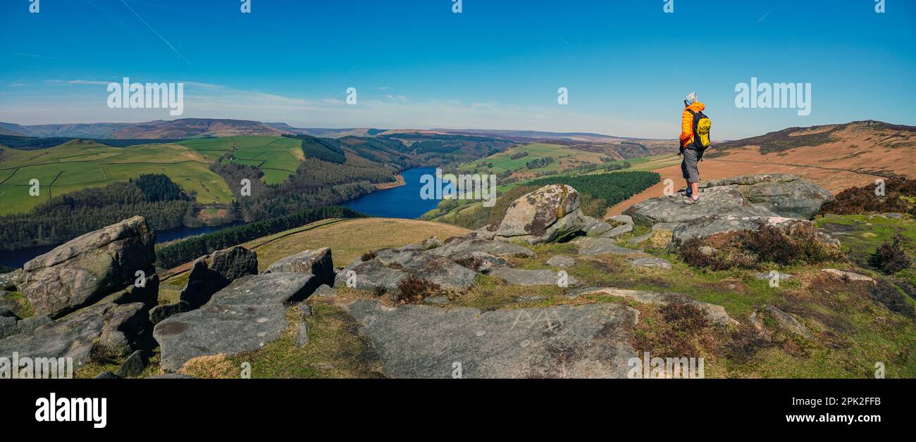 Escursionista femminile camminando lungo Dovestones Edge, sopra il lago artificiale di Ladybower e le dighe di Derwent, Peak District, Derbyshire, Regno Unito Foto Stock