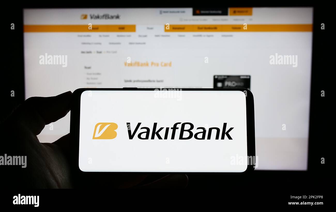 Persona in possesso di smartphone con logo di Turkiye Vakiflar Bankasi T.A.O. (VakifBank) sullo schermo davanti al sito web. Messa a fuoco sul display del telefono. Foto Stock