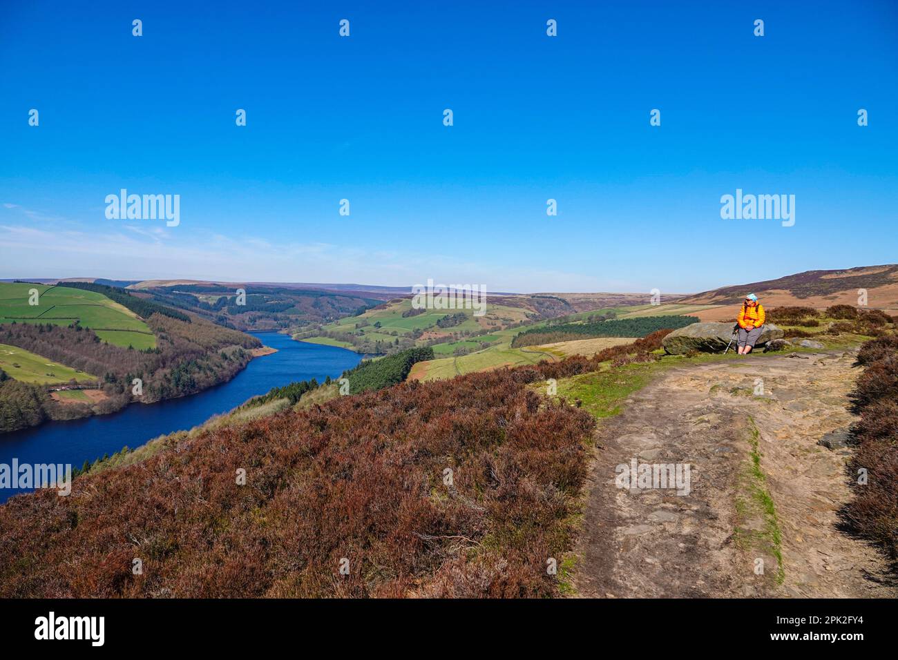 Escursionista femminile camminando lungo Dovestones Edge, sopra il lago artificiale di Ladybower e le dighe di Derwent, Peak District, Derbyshire, Regno Unito Foto Stock