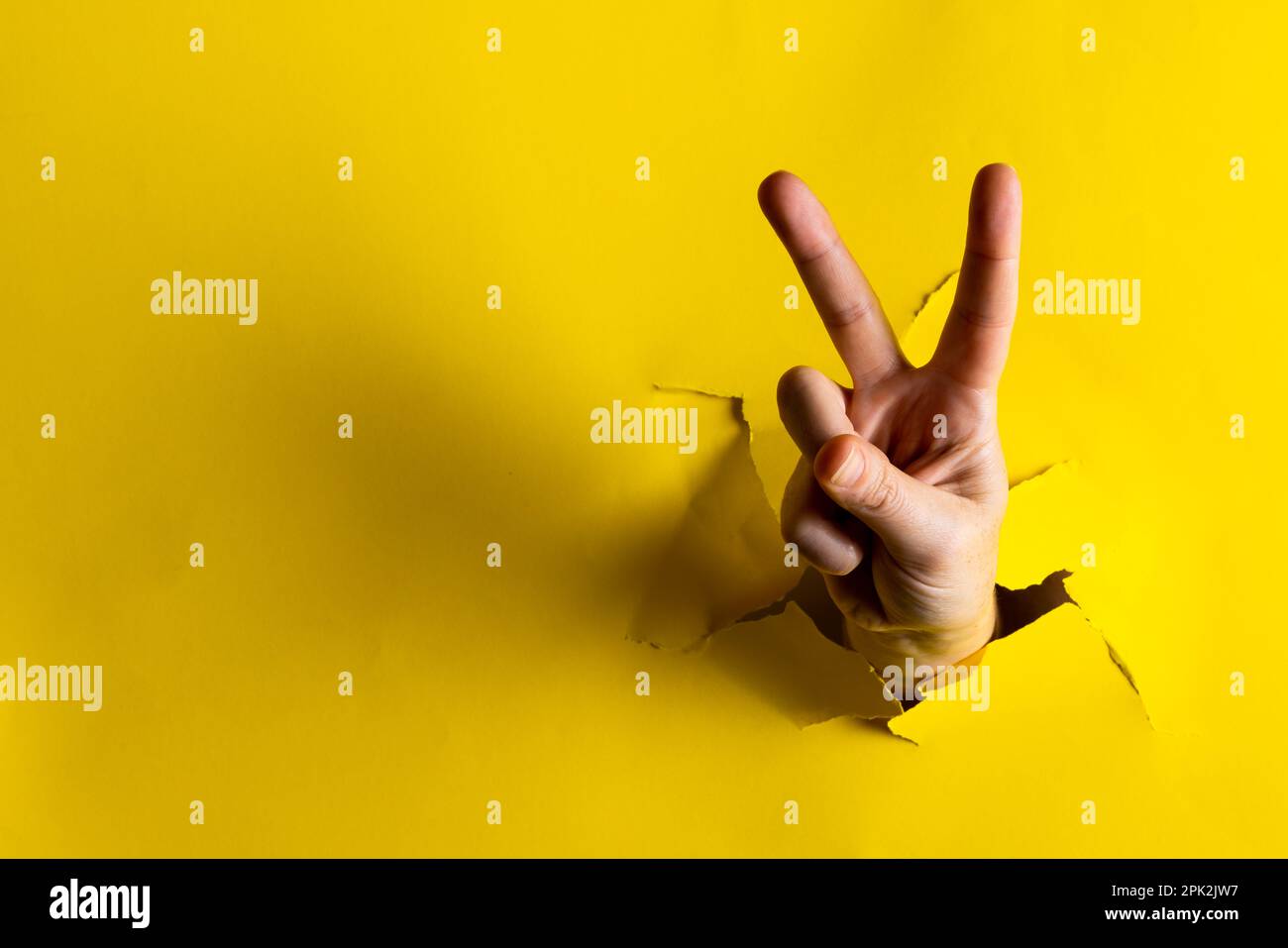 Primo piano di mano della donna caucasica che mostra un segno di pace con spazio copia su sfondo giallo lacerato Foto Stock
