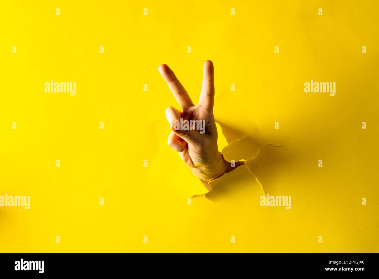 Primo piano di mano della donna caucasica che mostra un segno di pace con spazio copia su sfondo giallo lacerato Foto Stock