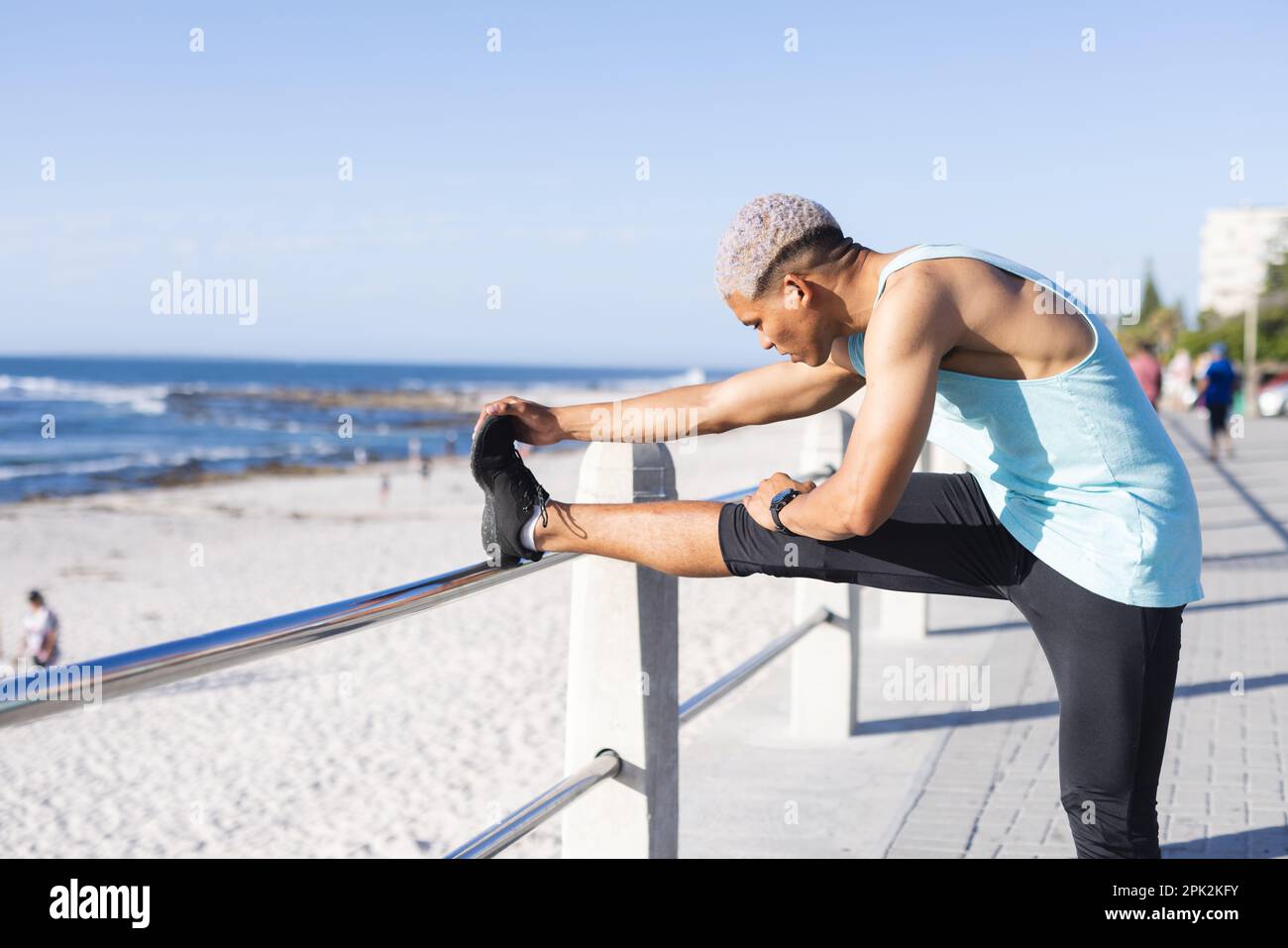 Uomo biraciale che indossa abbigliamento sportivo e che si estende sul lungomare sul mare Foto Stock