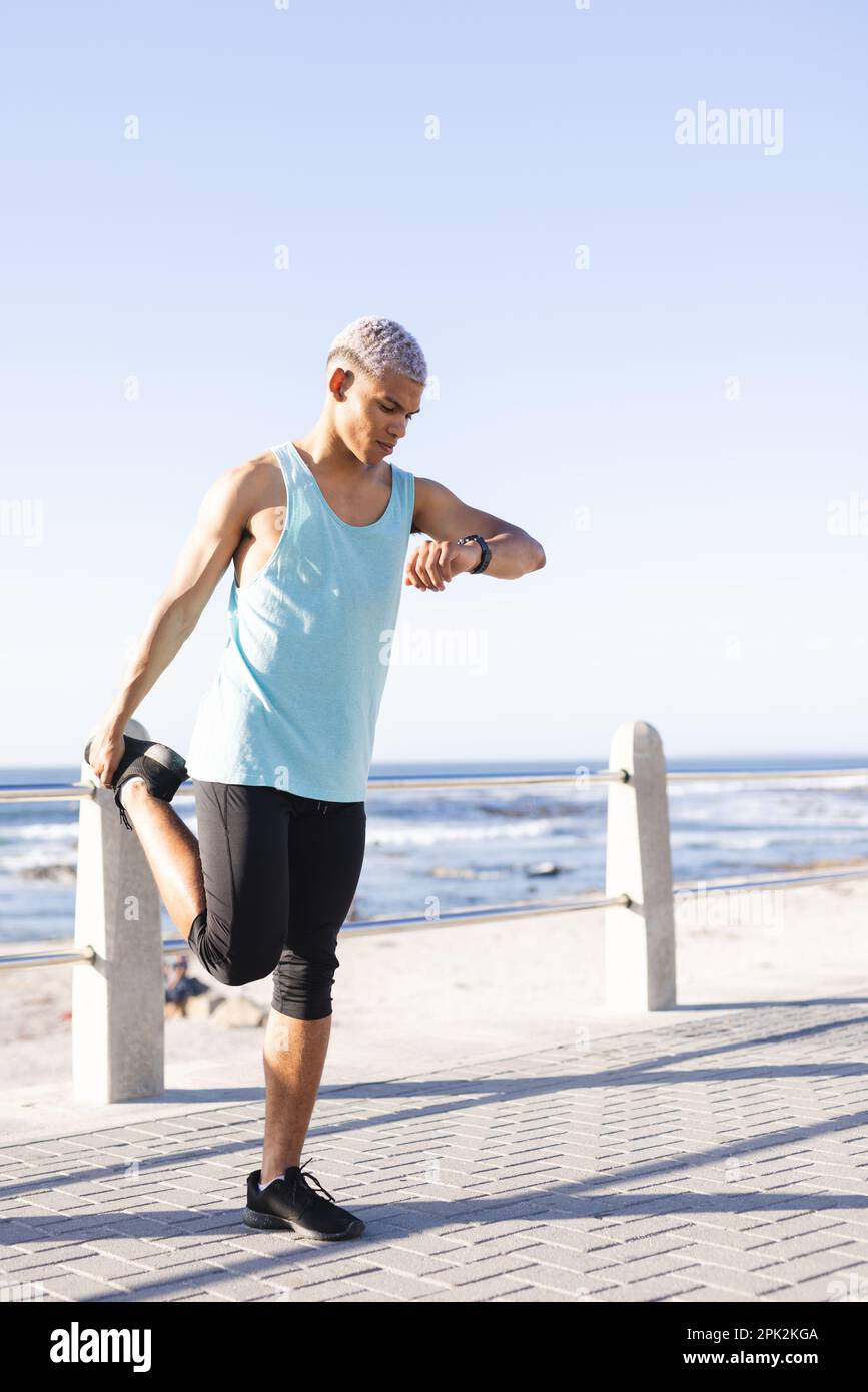Uomo biraciale che indossa abbigliamento sportivo e che si estende sul lungomare sul mare Foto Stock