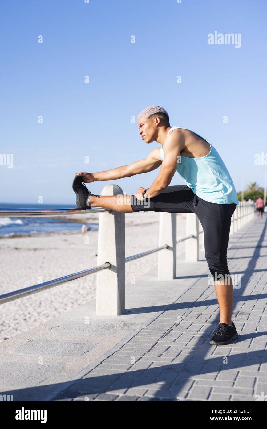 Uomo biraciale che indossa abbigliamento sportivo e che si estende sul lungomare sul mare Foto Stock