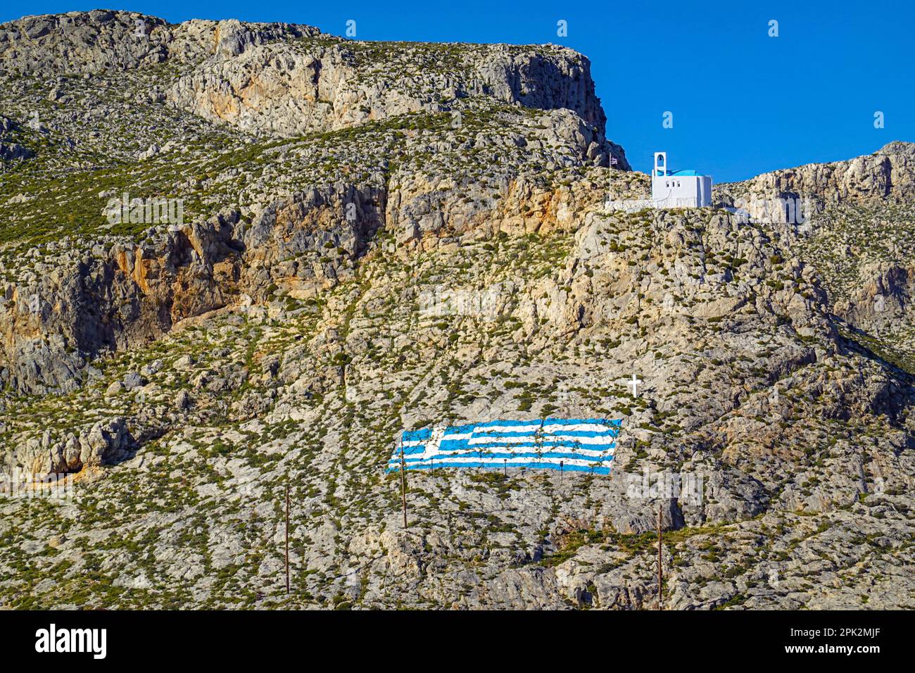 Cappella bianca e bandiera greca dipinta sulla collina sopra Pothia, la città principale di Kalymnos, isola greca, Isole Dodecanesi, Grecia Foto Stock