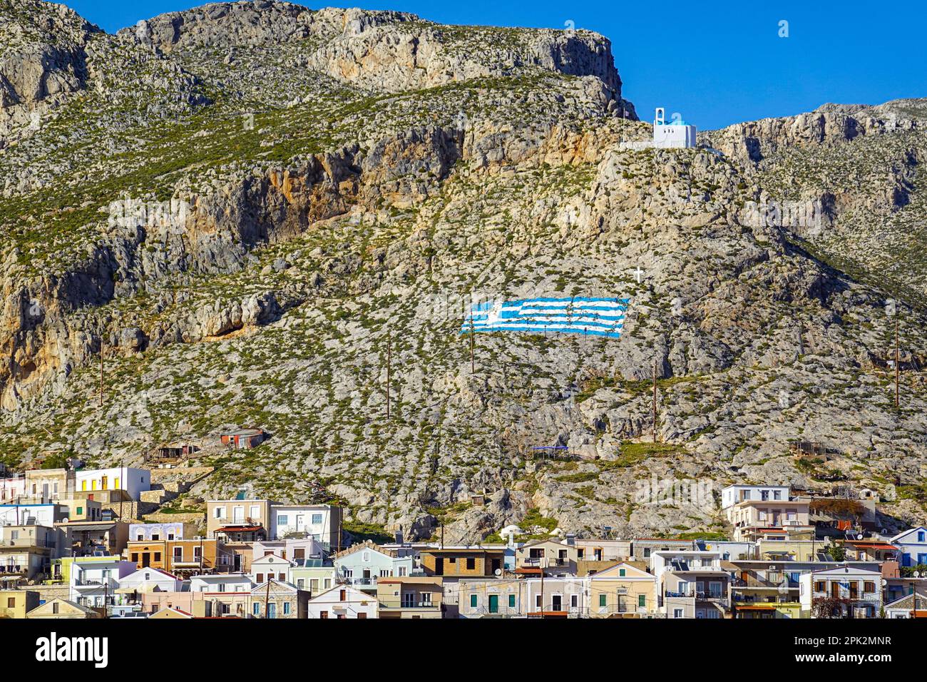 Cappella bianca e bandiera greca dipinta sulla collina sopra Pothia, la città principale di Kalymnos, isola greca, Isole Dodecanesi, Grecia Foto Stock