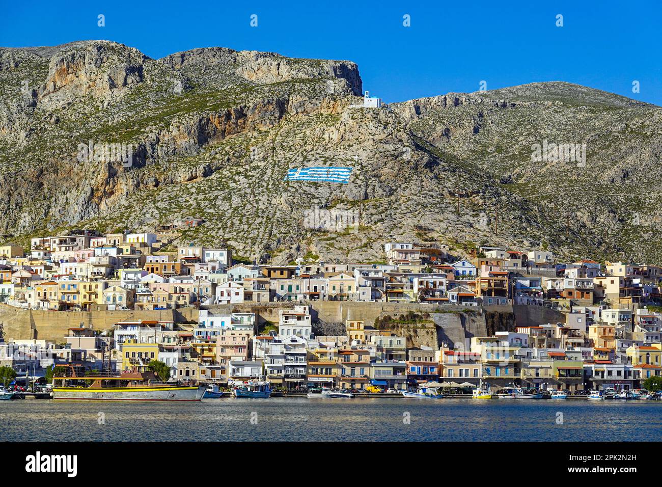 Cappella bianca e bandiera greca dipinta sulla collina sopra Pothia, la città principale di Kalymnos, isola greca, Isole Dodecanesi, Grecia Foto Stock